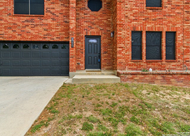 entrance to property featuring brick siding, a garage, and concrete driveway