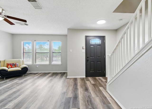 foyer with stairway, wood finished floors, a textured ceiling, baseboards, and visible vents