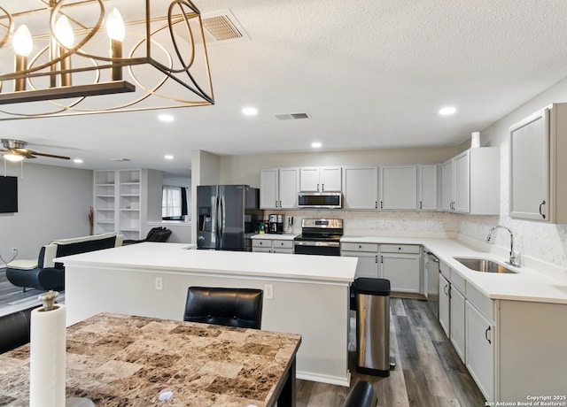 kitchen featuring a center island, a sink, visible vents, dark wood-type flooring, and appliances with stainless steel finishes