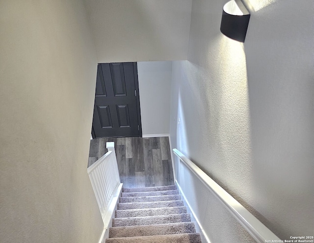 staircase featuring a textured wall, baseboards, and wood finished floors
