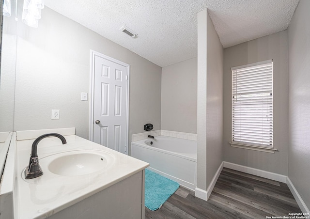 full bathroom featuring wood finished floors, visible vents, a sink, a bath, and a textured ceiling