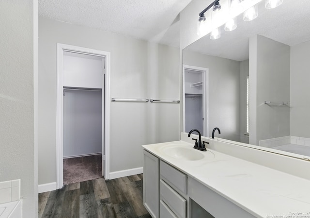 bathroom featuring a textured ceiling, baseboards, wood finished floors, vanity, and a walk in closet