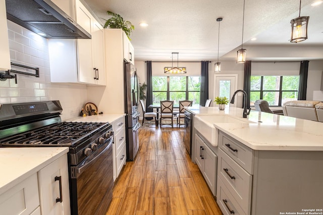 177 E Short Meadow Dr, Lytle, TX 78052 - kitchen featuring light wood-style flooring, a sink, range hood, light stone countertops, and appliances with stainless steel finishes