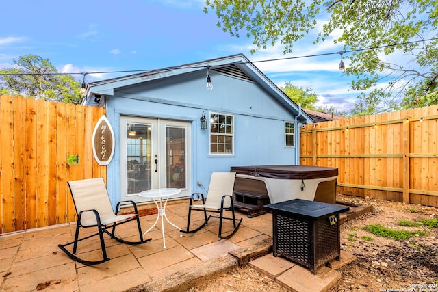 rear view of property with a fenced backyard, a hot tub, a patio, and french doors