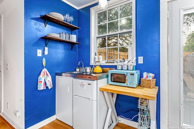 bar with baseboards, wood finished floors, white appliances, and a sink