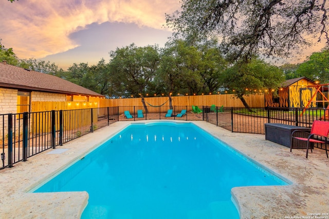 pool at dusk with fence, a patio, a fenced in pool, and a playground