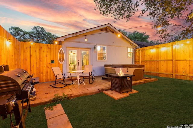 back of property at dusk featuring a fenced backyard, a fire pit, french doors, and a yard
