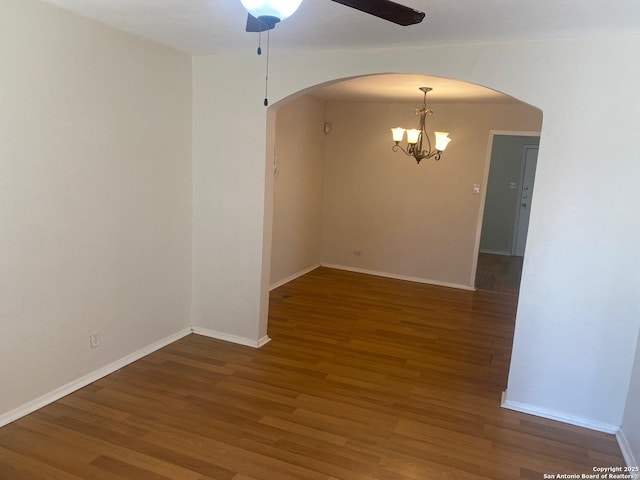 spare room with baseboards, arched walkways, wood finished floors, and ceiling fan with notable chandelier
