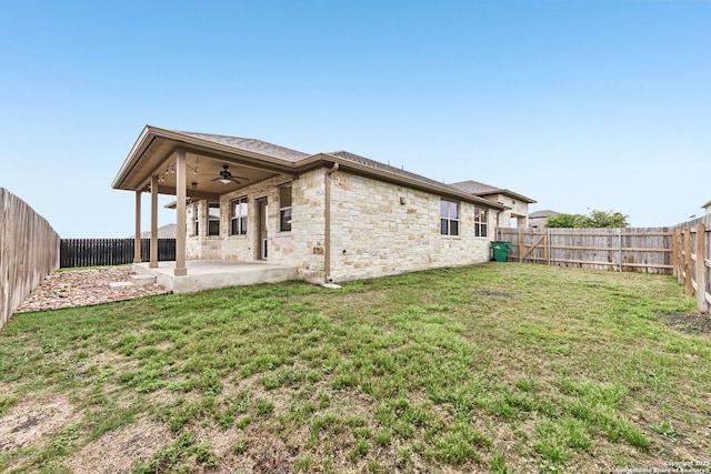 back of house with a patio area, a lawn, stone siding, a ceiling fan, and a fenced backyard
