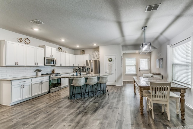 kitchen with stainless steel appliances, visible vents, dark wood-style floors, and a breakfast bar area