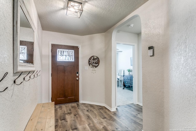 entryway with a textured wall, wood finished floors, arched walkways, and a textured ceiling