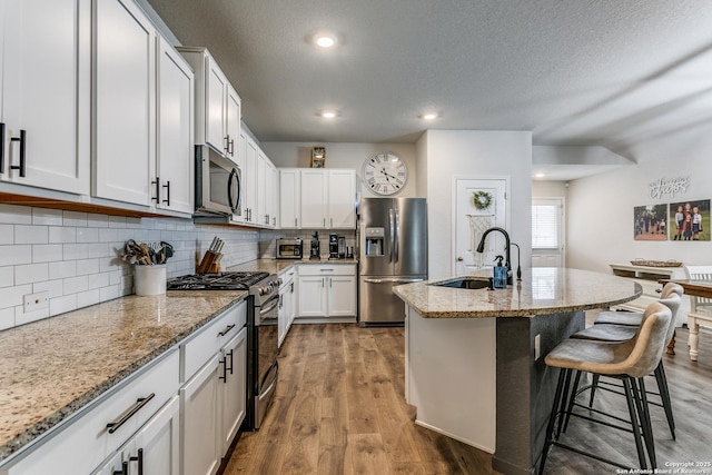 kitchen with wood finished floors, a sink, light stone countertops, appliances with stainless steel finishes, and a breakfast bar area