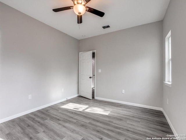 spare room with wood finished floors, visible vents, a ceiling fan, and baseboards