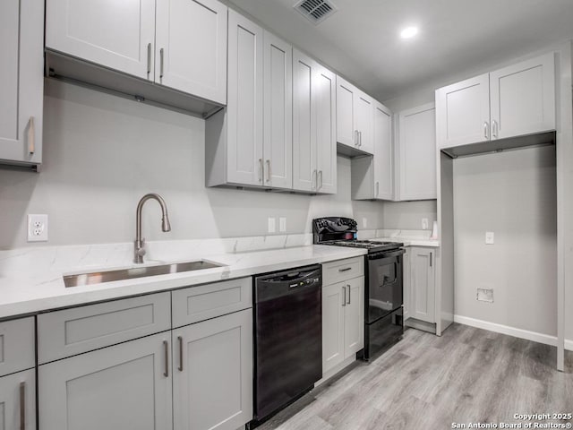 kitchen with a sink, black appliances, light wood-type flooring, baseboards, and visible vents