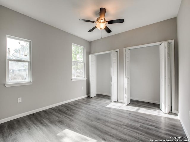 unfurnished bedroom featuring baseboards, a ceiling fan, wood finished floors, and two closets