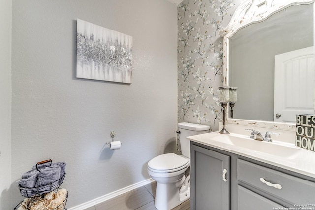bathroom with wallpapered walls, baseboards, toilet, and vanity