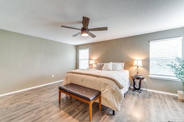 bedroom with a textured ceiling, light wood finished floors, baseboards, and ceiling fan