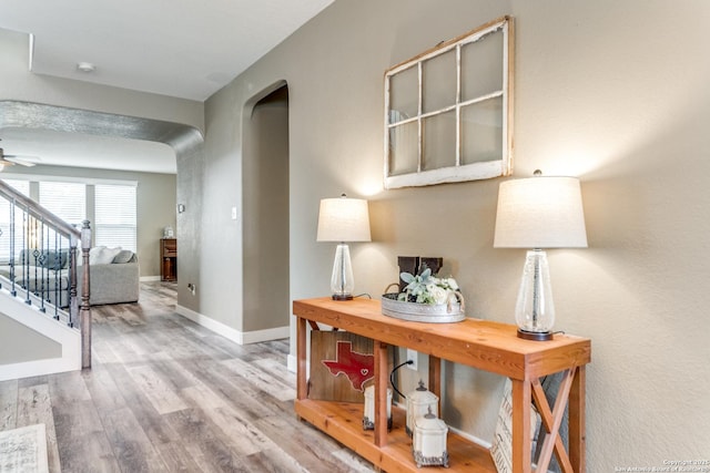 corridor featuring baseboards, wood finished floors, arched walkways, and stairs