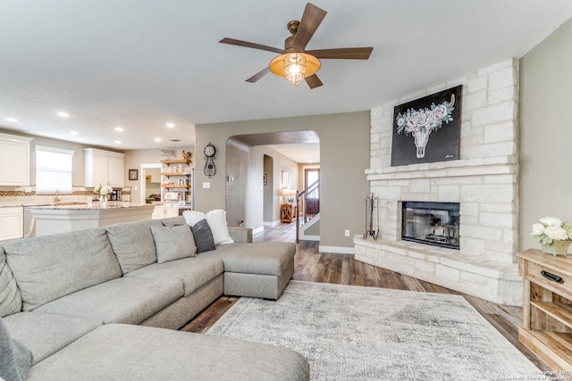 living area featuring arched walkways, baseboards, a ceiling fan, wood finished floors, and a fireplace