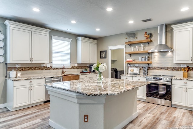 kitchen featuring wall chimney range hood, a sink, washer and dryer, decorative backsplash, and appliances with stainless steel finishes