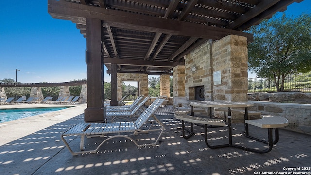 view of patio / terrace featuring a community pool, a pergola, fence, and an outdoor stone fireplace