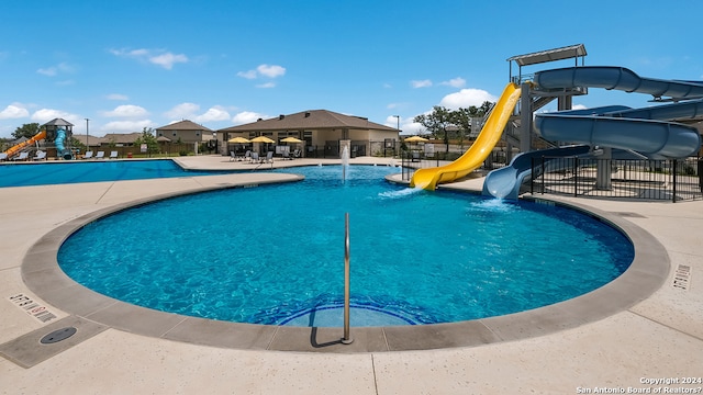 pool with playground community, a patio, a water slide, and fence