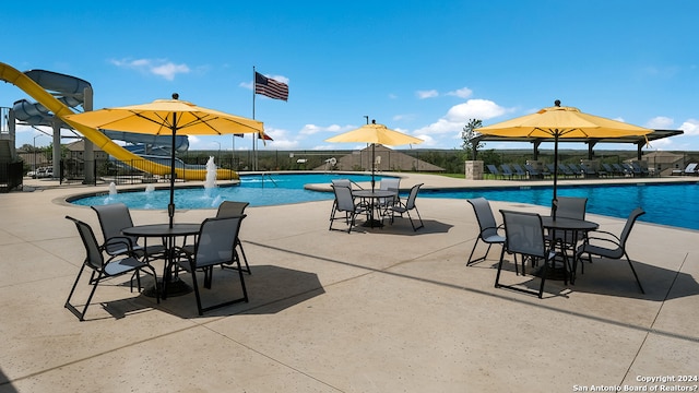pool with a patio area, fence, and a water slide