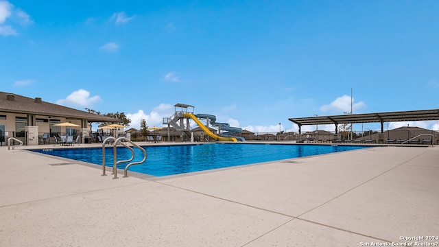 pool with a patio area, fence, a water slide, and playground community