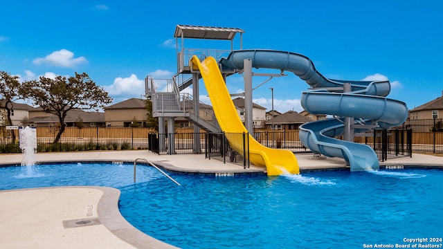 community pool with playground community, a water slide, and fence