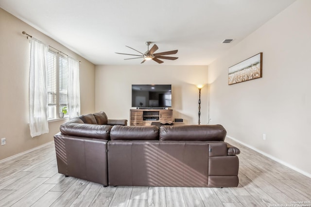 living room featuring baseboards, a ceiling fan, visible vents, and light wood-style floors