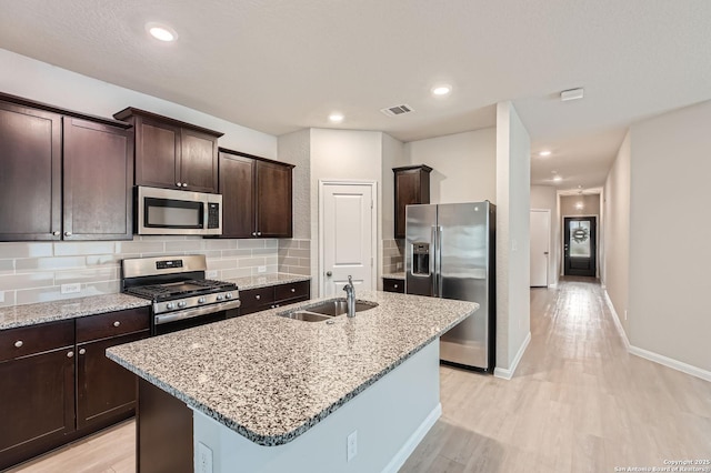5680 Jasmine Spur, Bulverde, TX 78163 - kitchen featuring appliances with stainless steel finishes, a sink, light wood-style floors, an island with sink, and dark brown cabinets