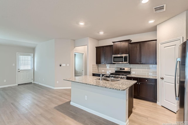5680 Jasmine Spur, Bulverde, TX 78163 - kitchen featuring appliances with stainless steel finishes, a sink, tasteful backsplash, light wood-style floors, and light stone counters