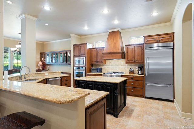 kitchen with custom exhaust hood, a sink, built in appliances, light stone countertops, and a kitchen island