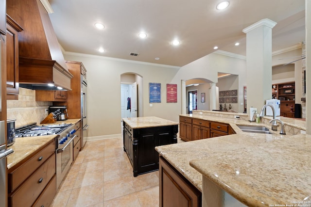 kitchen featuring arched walkways, ornamental molding, high end appliances, and decorative columns