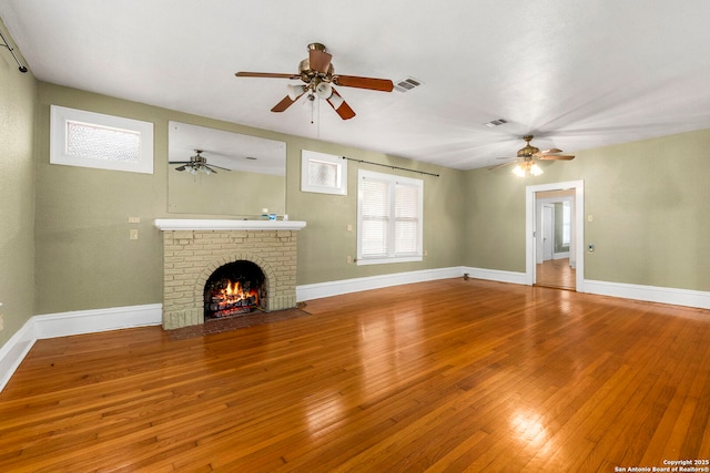 unfurnished living room with ceiling fan, a fireplace, wood-type flooring, baseboards, and visible vents