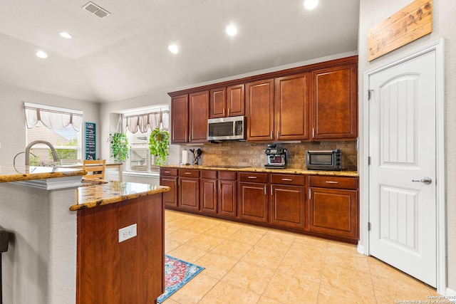 kitchen with black electric cooktop, stainless steel microwave, lofted ceiling, decorative backsplash, and light stone countertops