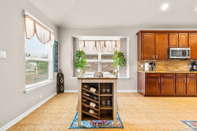 kitchen featuring brown cabinetry, decorative backsplash, stainless steel microwave, and light tile patterned flooring