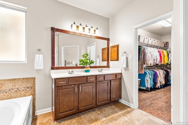full bath featuring a spacious closet, a garden tub, a sink, and double vanity