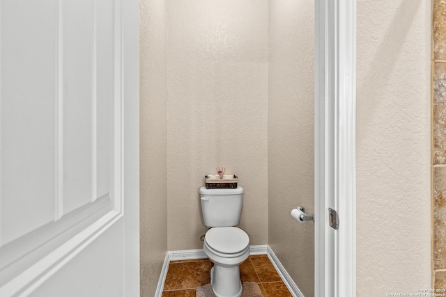 bathroom featuring tile patterned flooring, a textured wall, toilet, and baseboards