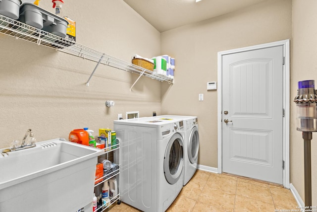 washroom with a sink, light tile patterned flooring, washer and dryer, baseboards, and laundry area