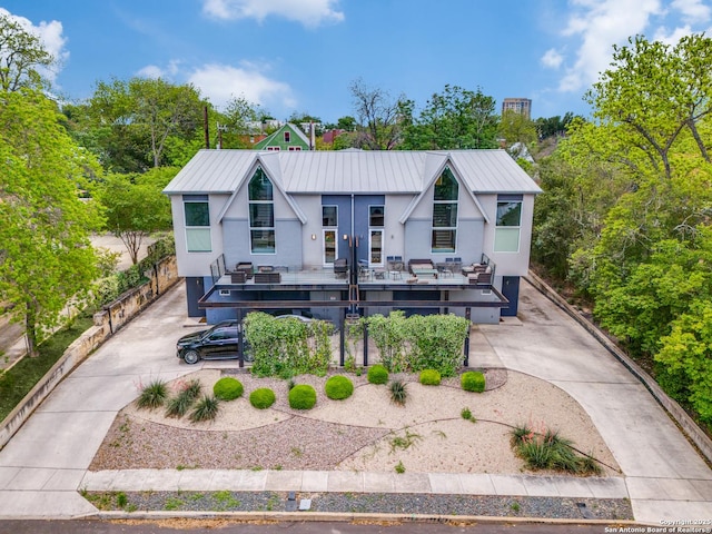 back of property featuring concrete driveway, stucco siding, a deck, and metal roof