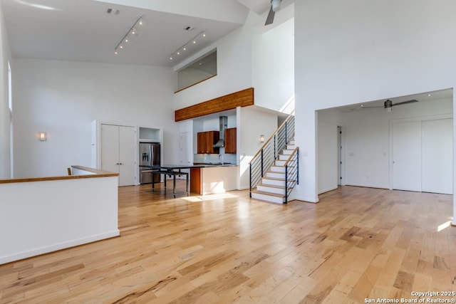 unfurnished living room featuring a towering ceiling, track lighting, a sink, light wood-style floors, and stairs