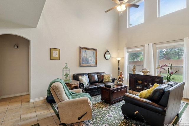 tiled living area featuring a ceiling fan, a high ceiling, arched walkways, and a healthy amount of sunlight
