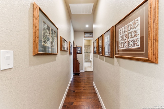 hallway featuring dark wood finished floors, baseboards, a textured wall, and visible vents