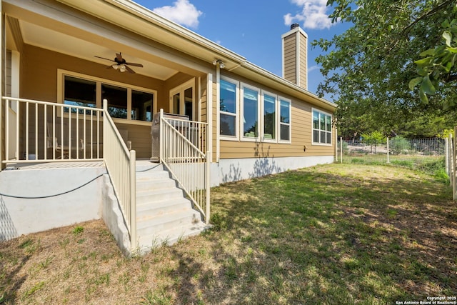 entrance to property with fence, ceiling fan, a chimney, and a yard