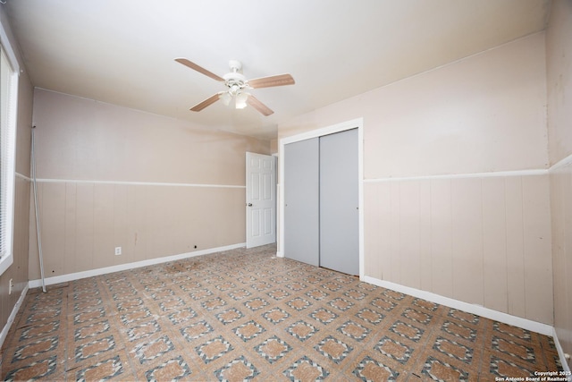unfurnished bedroom featuring a closet, baseboards, ceiling fan, and wainscoting