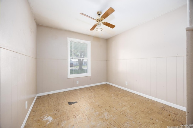 spare room with wainscoting, baseboards, and a ceiling fan