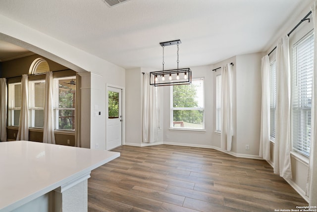 unfurnished dining area with baseboards, wood finished floors, and an inviting chandelier