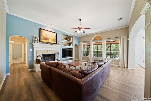 living area with wood finished floors, visible vents, a ceiling fan, arched walkways, and a fireplace