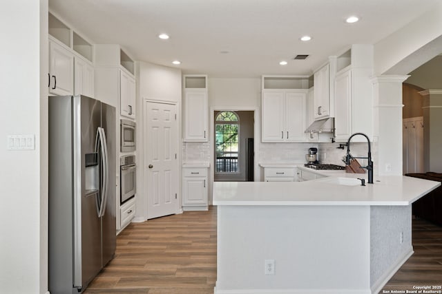 kitchen featuring stainless steel appliances, a peninsula, a sink, wood finished floors, and under cabinet range hood
